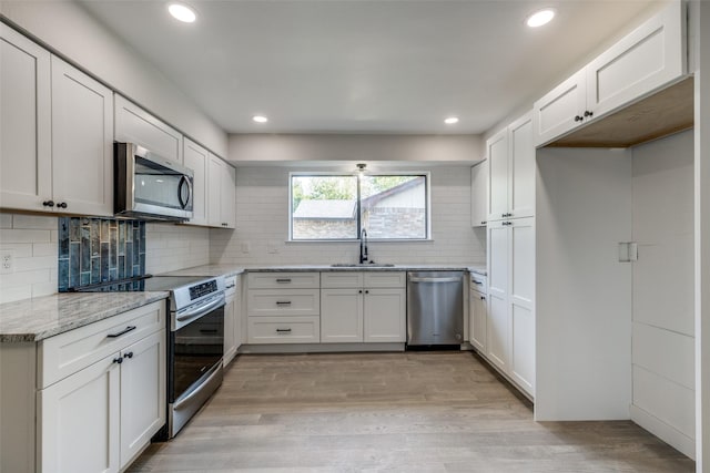 kitchen with stainless steel appliances, white cabinetry, light hardwood / wood-style floors, and sink