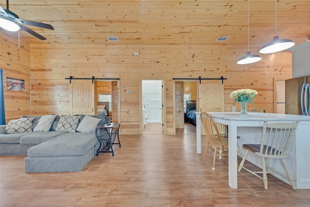 living room with a towering ceiling, a barn door, light hardwood / wood-style floors, and wood walls