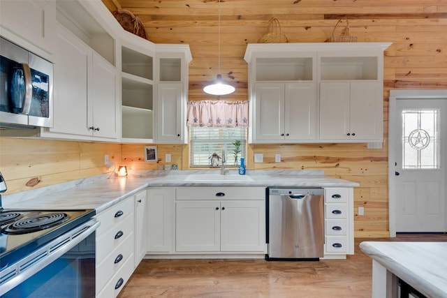 kitchen with pendant lighting, sink, wooden walls, appliances with stainless steel finishes, and white cabinetry