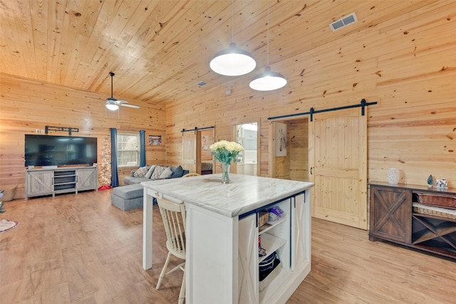 kitchen with pendant lighting, wooden walls, a barn door, light wood-type flooring, and wood ceiling