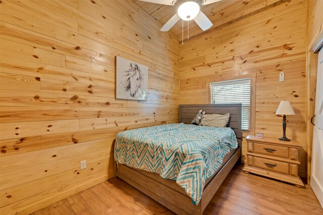 bedroom with hardwood / wood-style flooring, ceiling fan, and wood walls