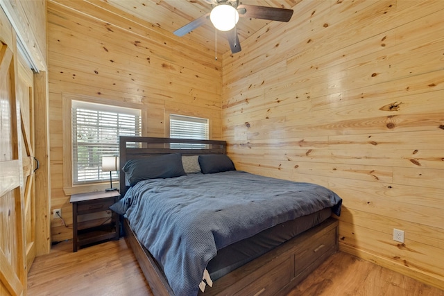 bedroom with light wood-type flooring, ceiling fan, and wooden walls