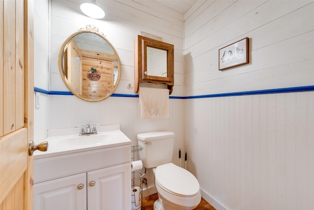 bathroom with vanity, toilet, and wood walls