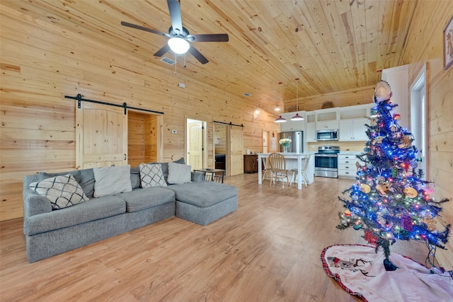 living room with ceiling fan, wooden ceiling, a barn door, wooden walls, and light wood-type flooring