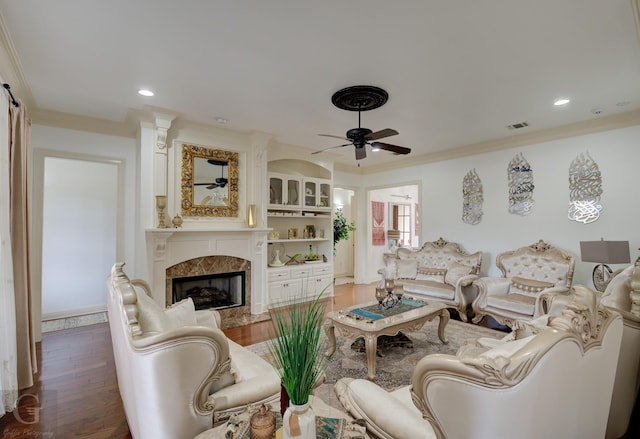 living room featuring a high end fireplace, dark wood-type flooring, ornamental molding, and ceiling fan