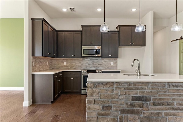 kitchen with decorative light fixtures, a barn door, sink, a kitchen island with sink, and appliances with stainless steel finishes