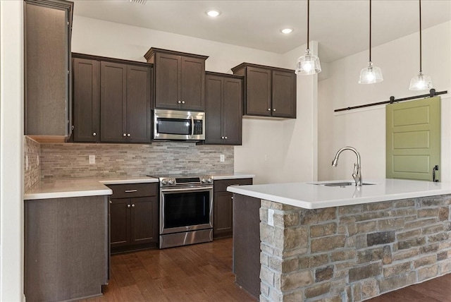 kitchen featuring pendant lighting, stainless steel appliances, sink, dark brown cabinets, and a barn door