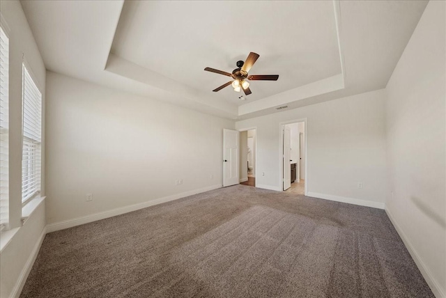 carpeted spare room with a raised ceiling and ceiling fan