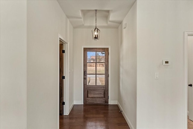 doorway to outside featuring dark hardwood / wood-style flooring, a raised ceiling, and a notable chandelier