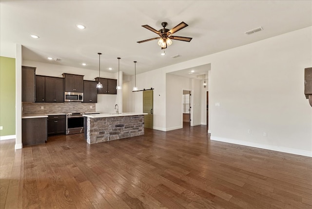 kitchen with decorative light fixtures, sink, dark brown cabinetry, a kitchen island with sink, and appliances with stainless steel finishes