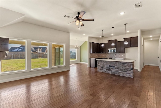 kitchen with tasteful backsplash, vaulted ceiling, hanging light fixtures, an island with sink, and dark brown cabinets