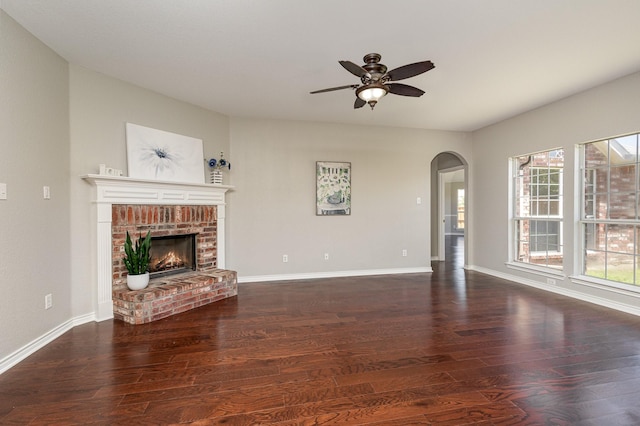 unfurnished living room featuring ceiling fan, dark hardwood / wood-style floors, and a brick fireplace