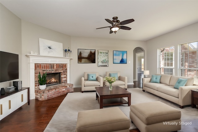 living room featuring ceiling fan, wood-type flooring, and a brick fireplace