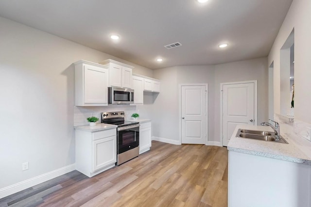 kitchen with tasteful backsplash, appliances with stainless steel finishes, white cabinets, and light hardwood / wood-style floors