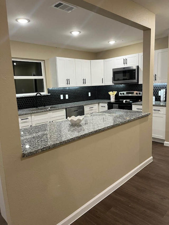 kitchen with stainless steel appliances, dark wood-type flooring, sink, dark stone countertops, and white cabinetry