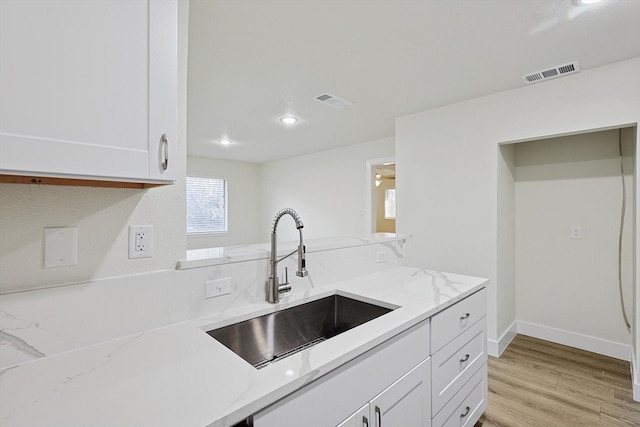 kitchen featuring light stone countertops, light hardwood / wood-style flooring, white cabinetry, and sink