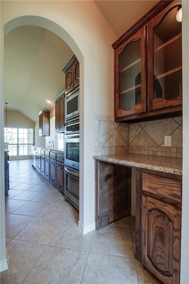 kitchen featuring lofted ceiling, light tile patterned floors, appliances with stainless steel finishes, backsplash, and light stone countertops