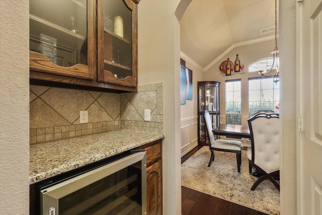 bar with vaulted ceiling, beverage cooler, crown molding, light stone countertops, and dark wood-type flooring