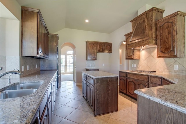 kitchen featuring stainless steel gas stovetop, lofted ceiling, sink, and light stone counters