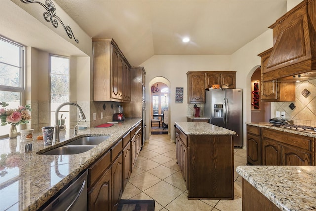 kitchen with sink, light stone counters, a center island, appliances with stainless steel finishes, and custom range hood