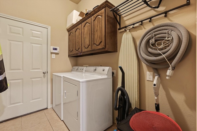 clothes washing area with cabinets, washing machine and clothes dryer, and light tile patterned floors