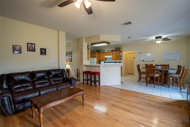 living room with ceiling fan, a textured ceiling, and light hardwood / wood-style flooring