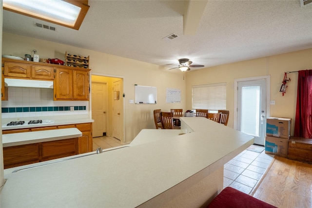 kitchen with white gas cooktop, ceiling fan, light wood-type flooring, a textured ceiling, and tasteful backsplash