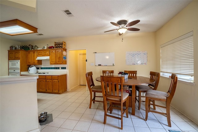 tiled dining area with a textured ceiling and ceiling fan