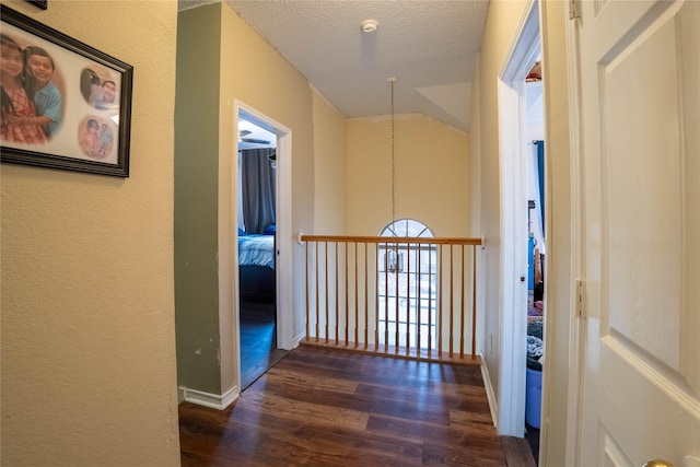 hallway featuring a textured ceiling, dark hardwood / wood-style flooring, and vaulted ceiling