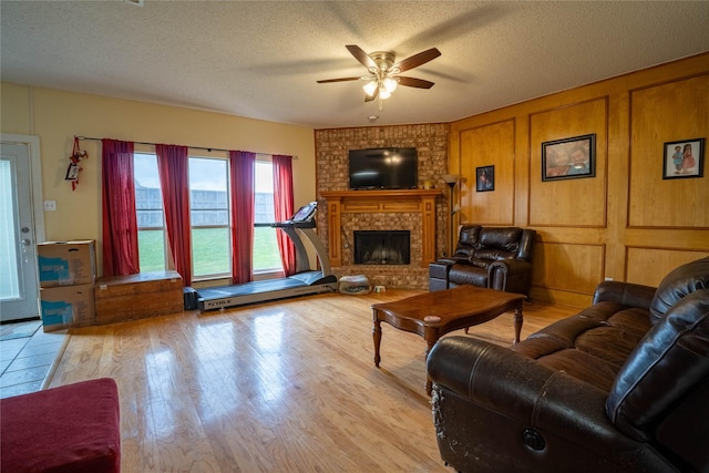 living room with ceiling fan, light hardwood / wood-style floors, a textured ceiling, and a brick fireplace