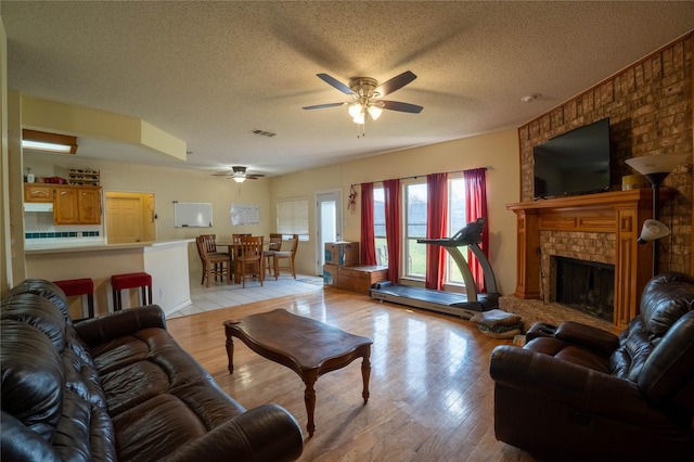 living room featuring ceiling fan, light hardwood / wood-style floors, a textured ceiling, and a brick fireplace