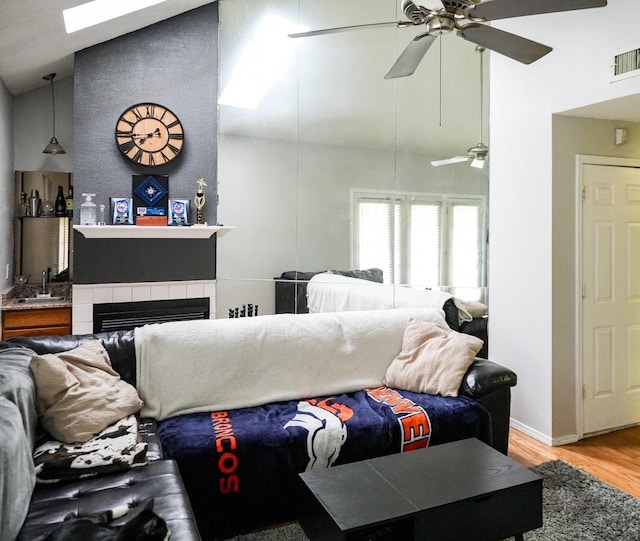 living room featuring sink, light hardwood / wood-style flooring, a tile fireplace, ceiling fan, and high vaulted ceiling