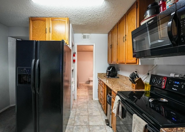 kitchen with black appliances, light stone counters, light tile patterned floors, and a textured ceiling