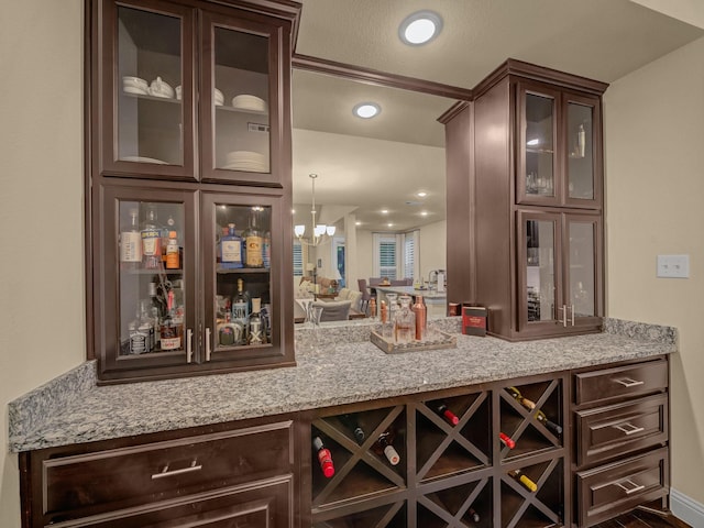 bar featuring an inviting chandelier, light stone countertops, dark brown cabinets, and pendant lighting