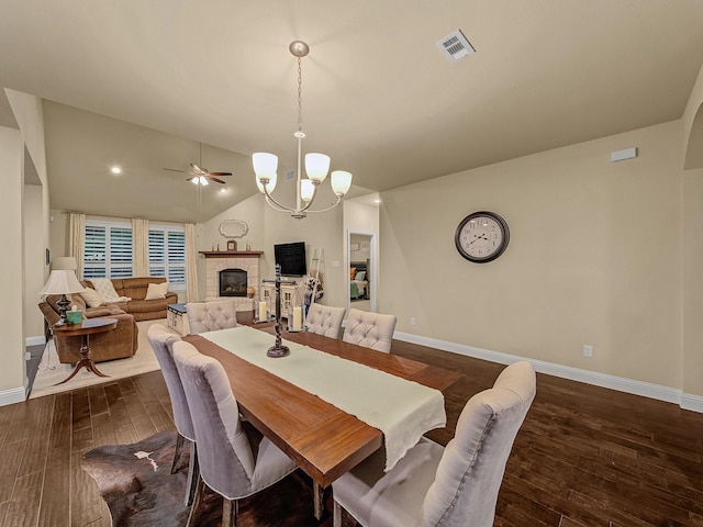 dining room with lofted ceiling, a fireplace, dark hardwood / wood-style flooring, and ceiling fan with notable chandelier