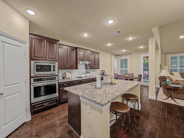 kitchen featuring an island with sink, appliances with stainless steel finishes, a breakfast bar, and dark wood-type flooring