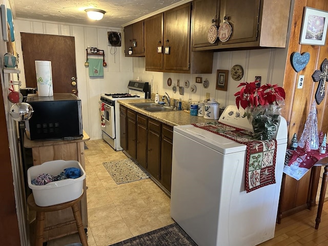 kitchen featuring white range with gas stovetop, dark brown cabinetry, washer / clothes dryer, and sink