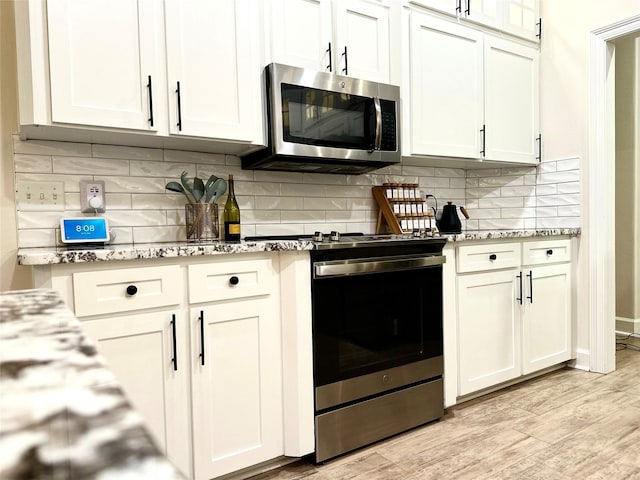 kitchen with stainless steel appliances, light stone counters, backsplash, light hardwood / wood-style floors, and white cabinets