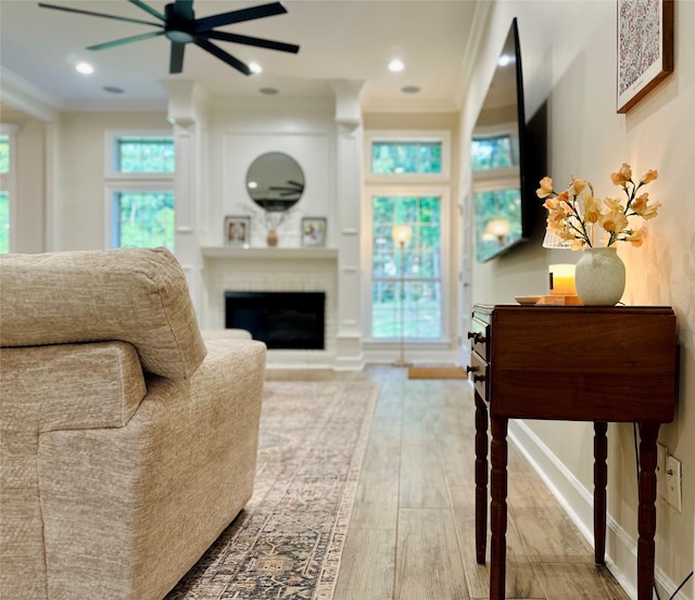 living room with hardwood / wood-style flooring, ceiling fan, ornamental molding, and a brick fireplace