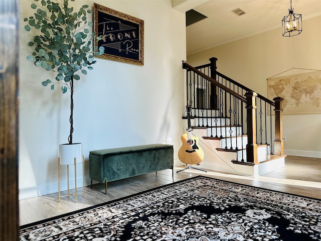 stairway with hardwood / wood-style floors, crown molding, and an inviting chandelier