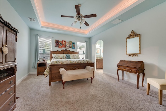 carpeted bedroom with ensuite bathroom, crown molding, ceiling fan, and a tray ceiling