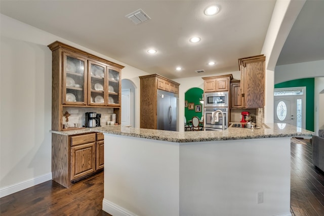 kitchen featuring built in appliances, decorative backsplash, dark hardwood / wood-style floors, light stone counters, and kitchen peninsula