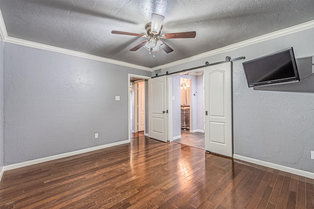 unfurnished bedroom featuring ceiling fan, a barn door, dark hardwood / wood-style flooring, crown molding, and a textured ceiling