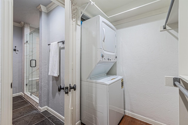 laundry room with dark tile patterned flooring, crown molding, and stacked washer and clothes dryer