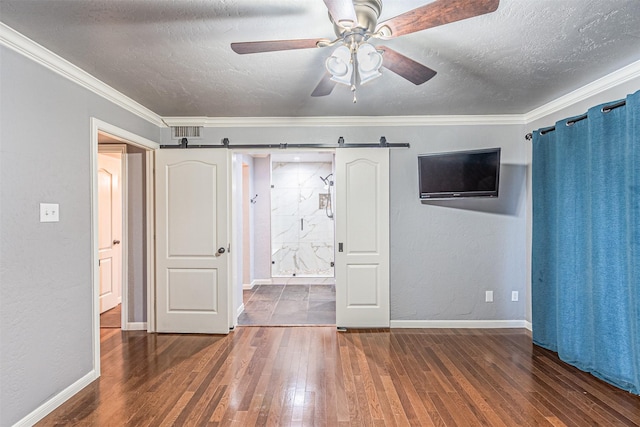 unfurnished bedroom featuring a barn door, dark wood-type flooring, ceiling fan, and crown molding