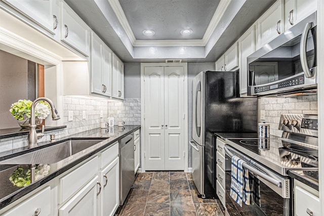 kitchen featuring white cabinets, ornamental molding, a tray ceiling, stainless steel appliances, and a sink