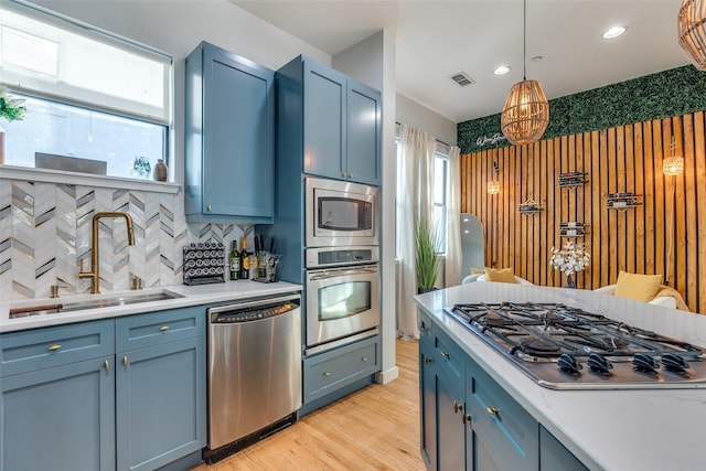 kitchen with decorative light fixtures, blue cabinets, sink, stainless steel appliances, and light hardwood / wood-style flooring