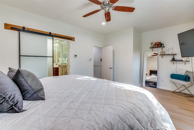 bedroom with a barn door, light wood-type flooring, connected bathroom, and ceiling fan