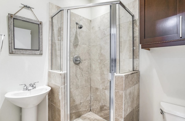 bathroom featuring a shower with door, sink, and toilet