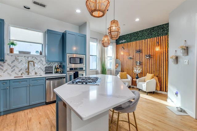 kitchen with a kitchen island, appliances with stainless steel finishes, decorative light fixtures, sink, and decorative backsplash